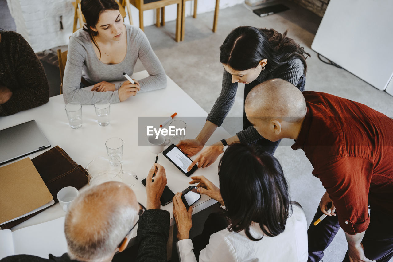 High angle view of female hacker discussing over smart phone with advisors at office