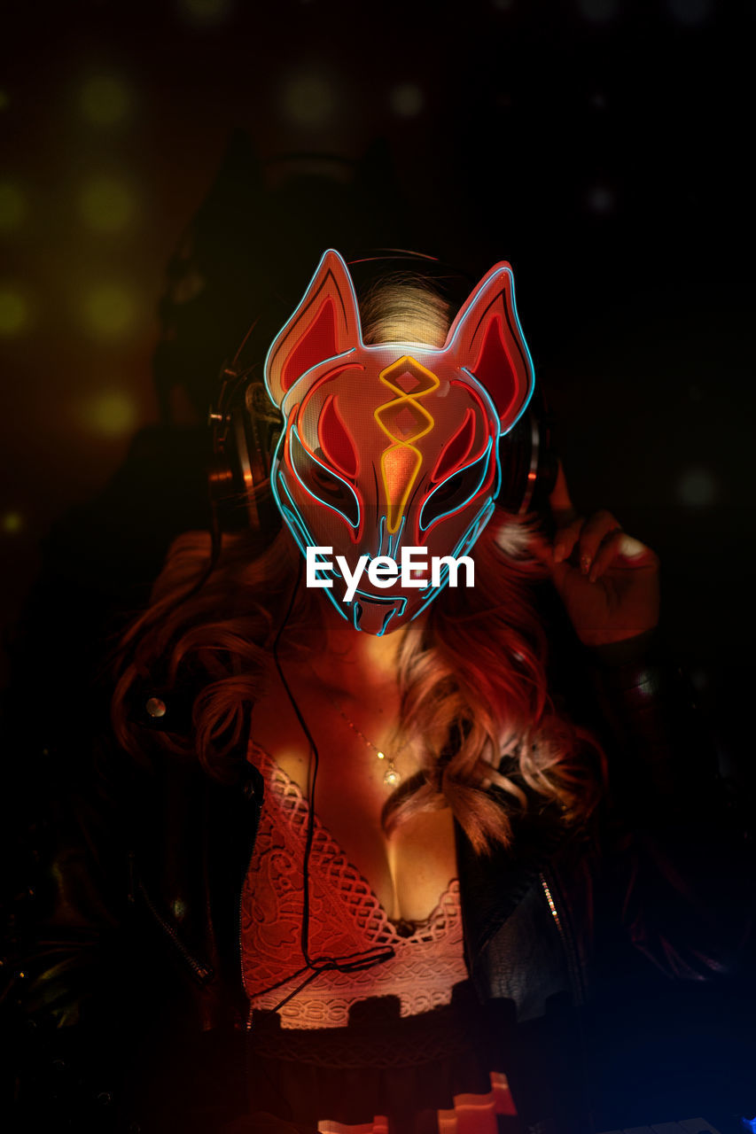 Anonymous woman in creative fox mask with neon ornaments working during party in nightclub