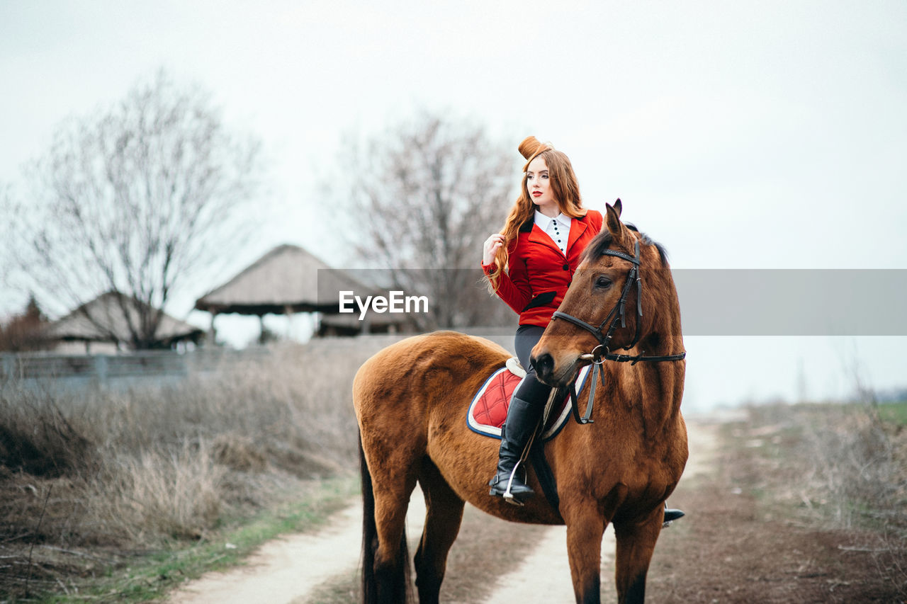 PERSON RIDING HORSE ON FIELD AGAINST SKY