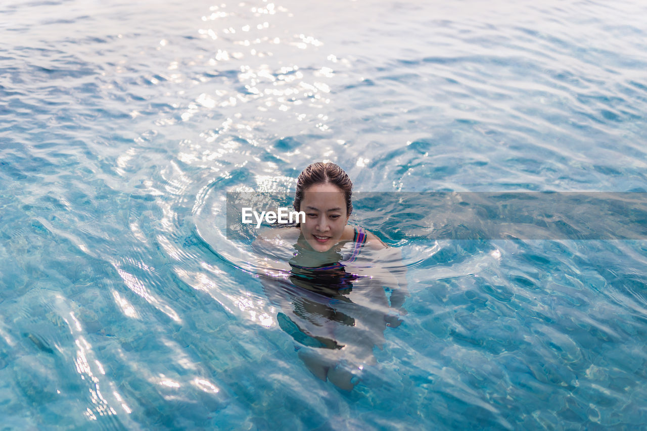 High angle portrait of smiling woman swimming in pool