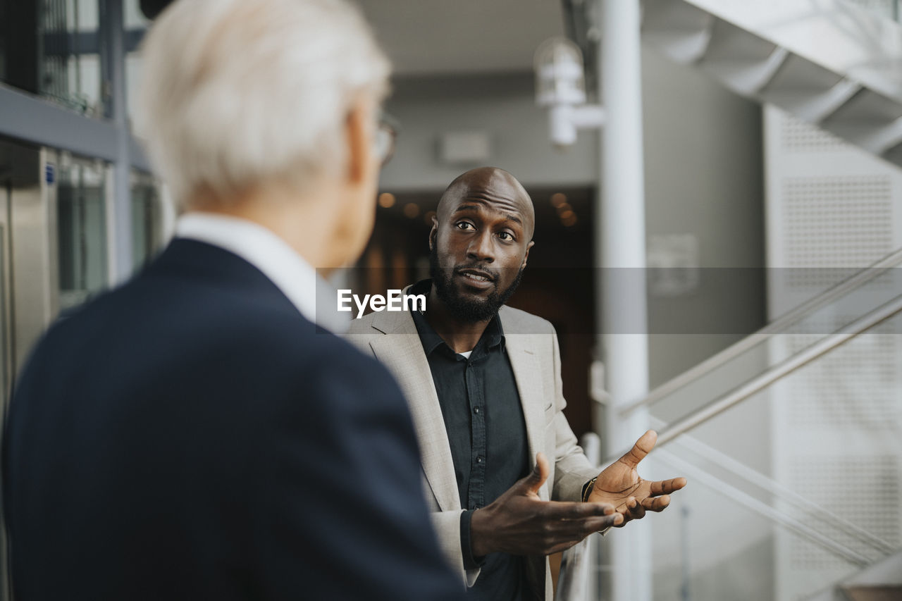 Bald businessman gesturing while discussing with senior male colleague
