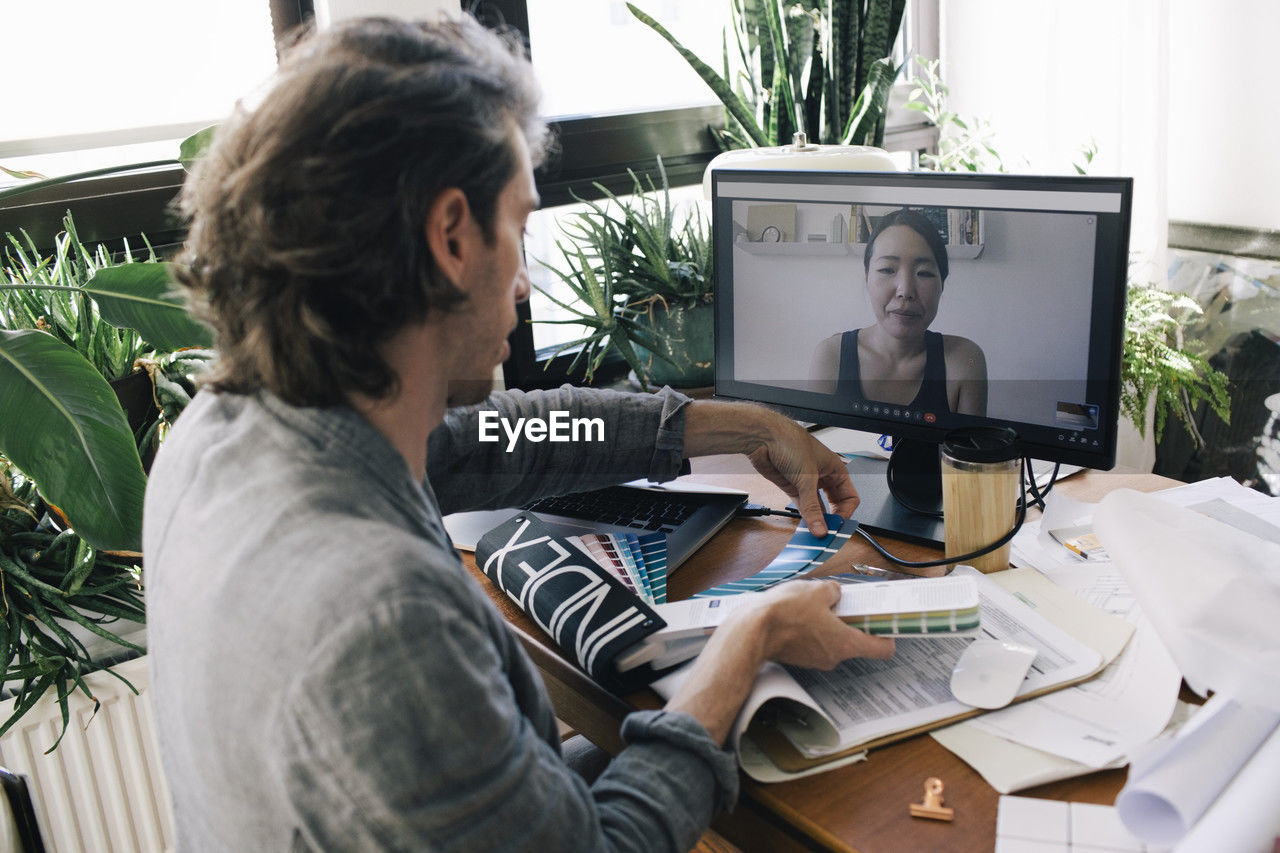 Male architect on video call with female coworker through computer discussing over color swatch at home office