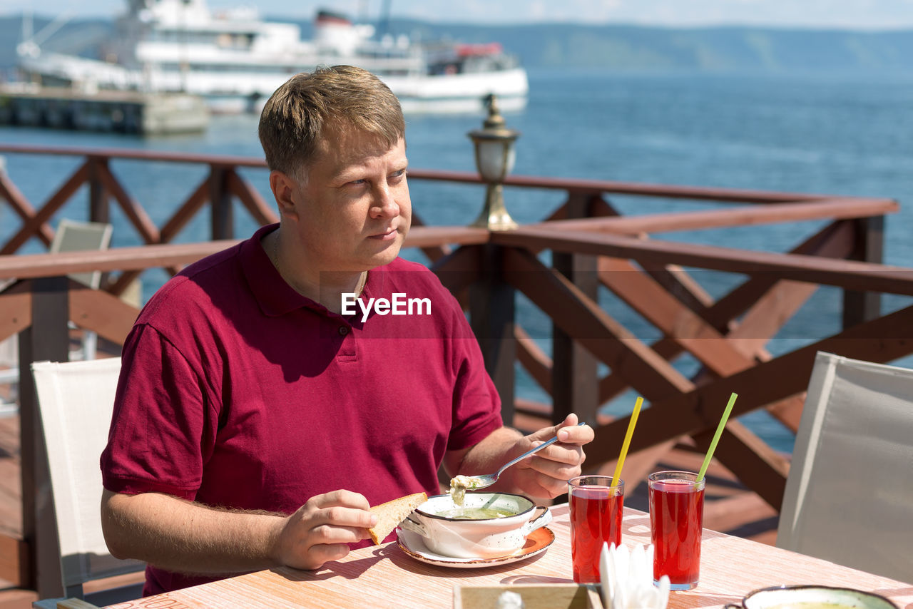 An adult blonde man has lunch on the beach in a cafe in the fresh air.