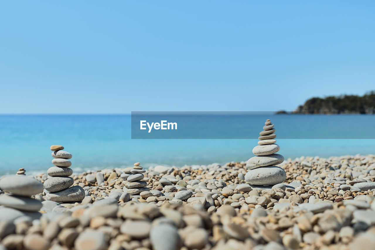 Pyramid stones balance on the beach against the background of the sea and the sky. 