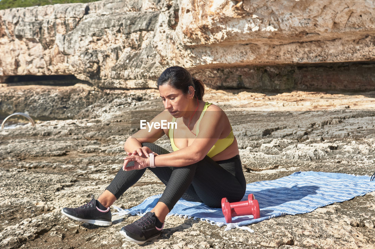 Latin woman, middle-aged, looking at app, smart watch, resting after gym session, 