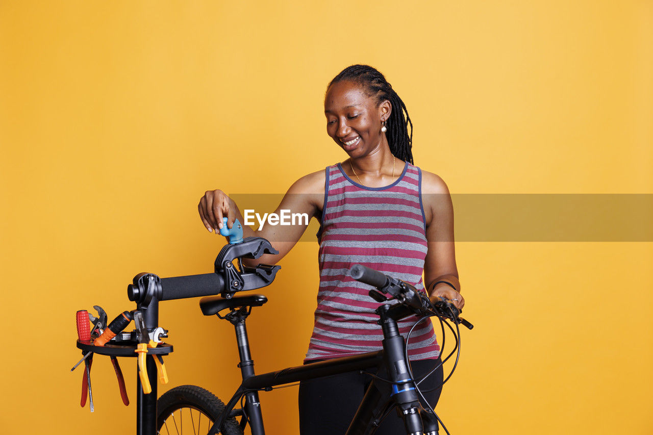 portrait of young woman with bicycle against yellow background