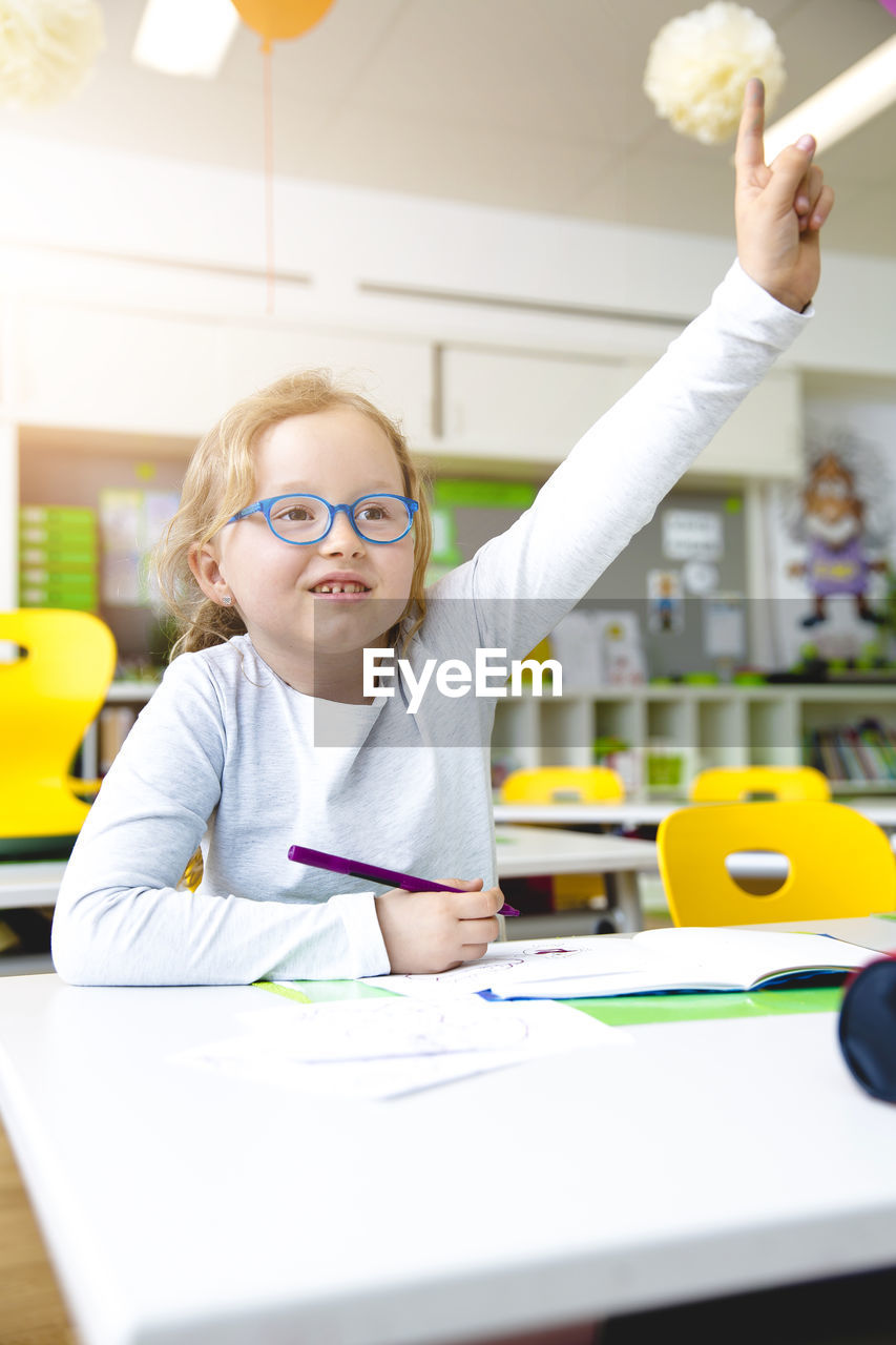 Girl with hand raised sitting at desk in classroom
