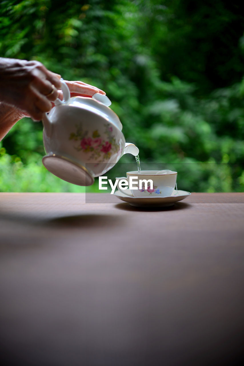 Hand serving tea on a wooden table against green nature