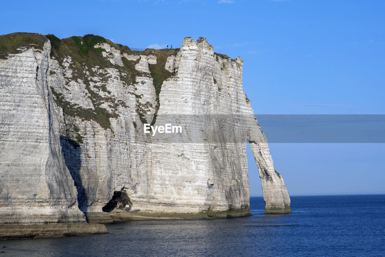 Rock formation by sea against clear blue sky