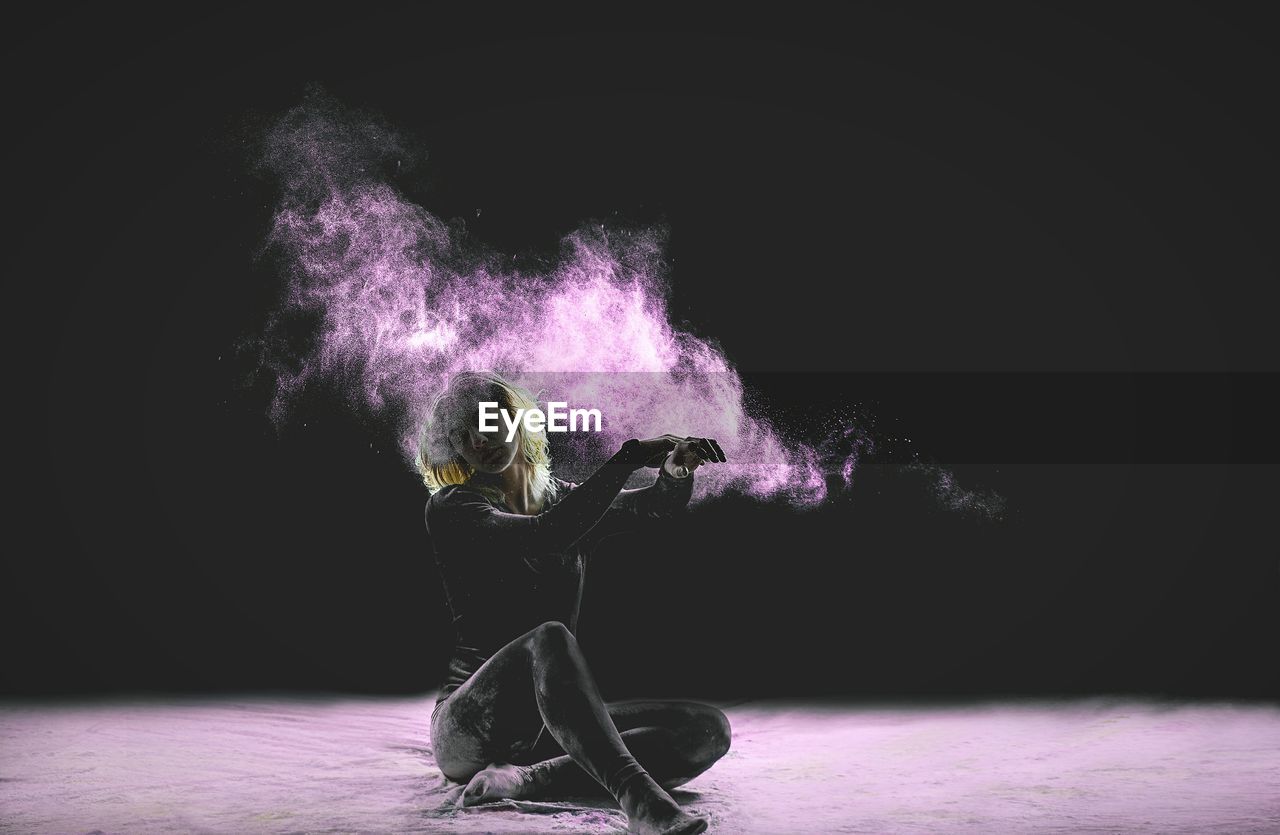 Young female dancer performing with powder against black background