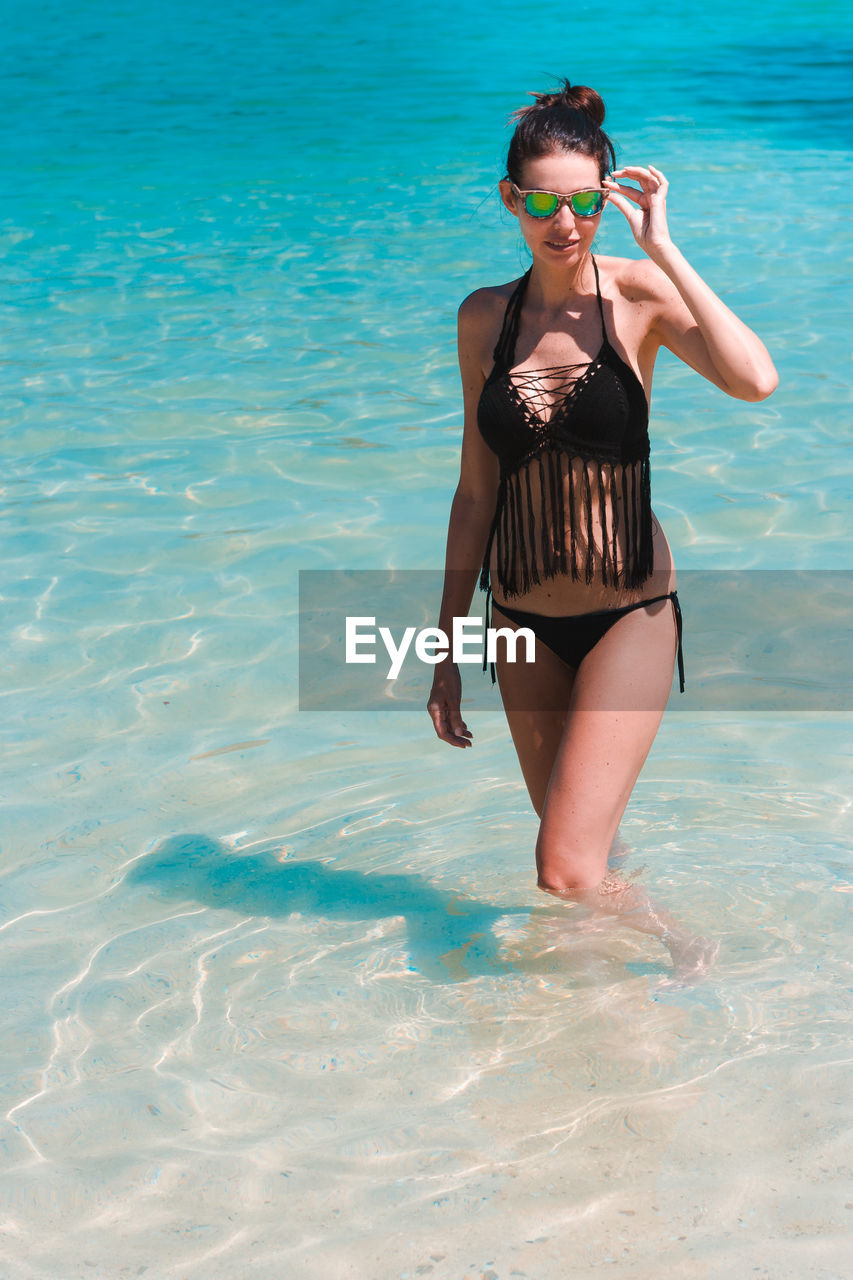 Woman wearing bikini and sunglasses standing in sea during summer