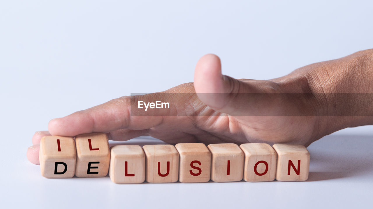 Hand holding dice with text for illustration of illusion and delusion words