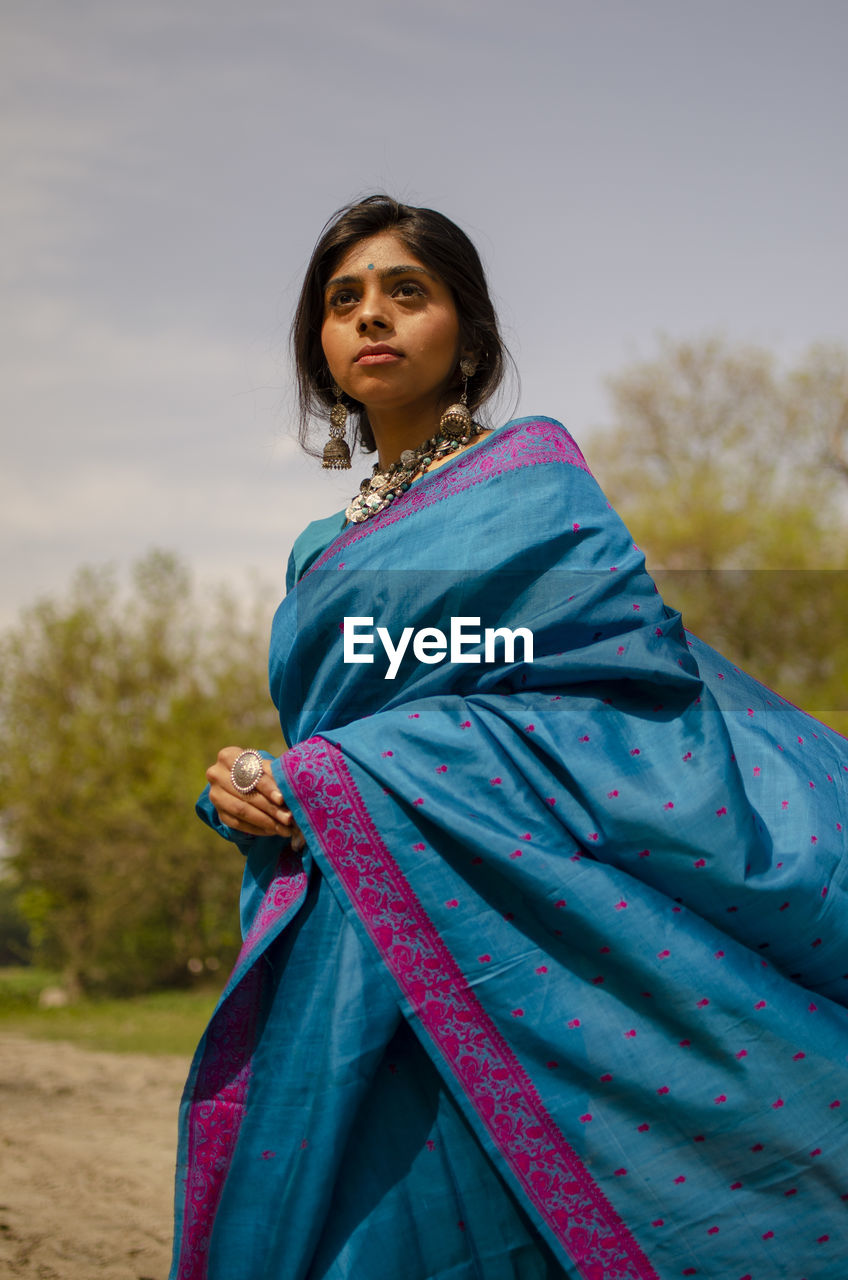 Low angle view of young woman wearing sari standing against sky