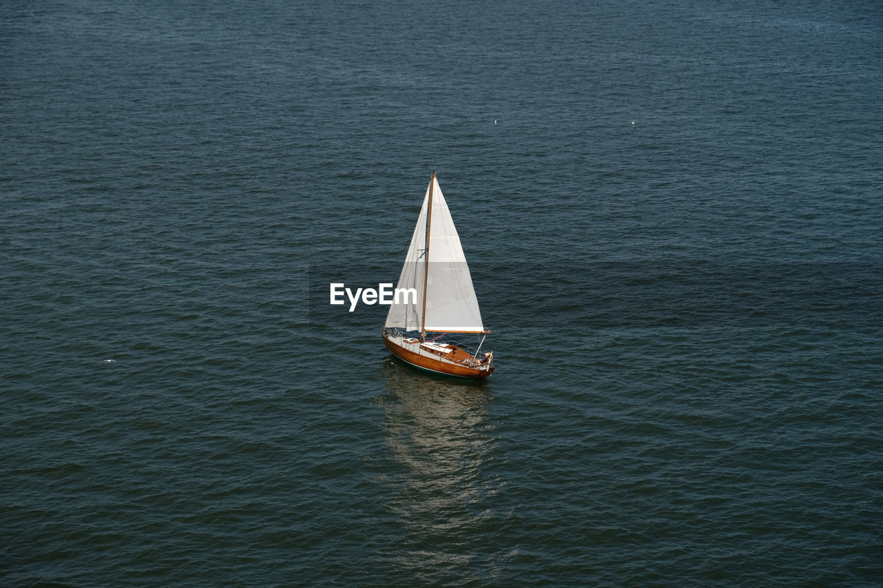 Aerial view of wooden old yacht with sail, blue water with waves and ripples. lonely white sail 