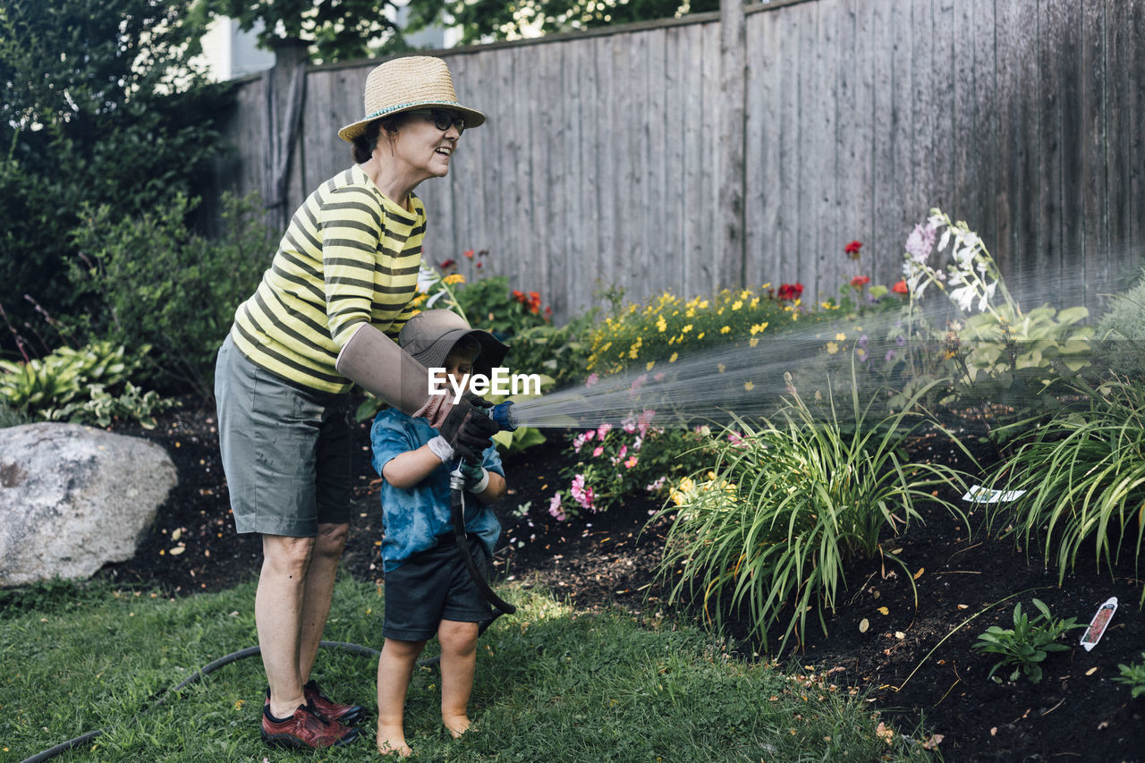 Happy grandmother with grandson watering plants together in garden