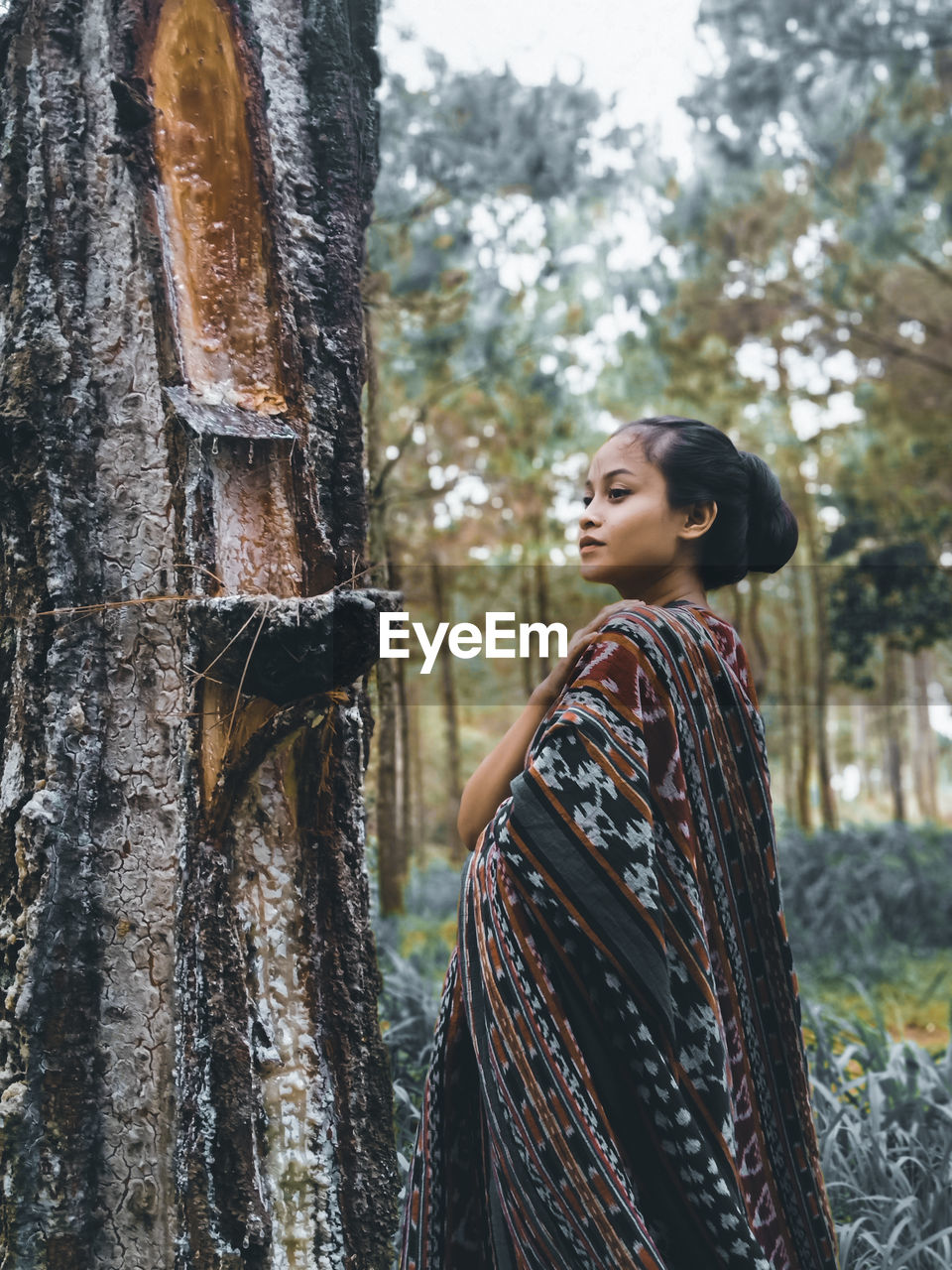 Side view of young woman looking at tree trunk