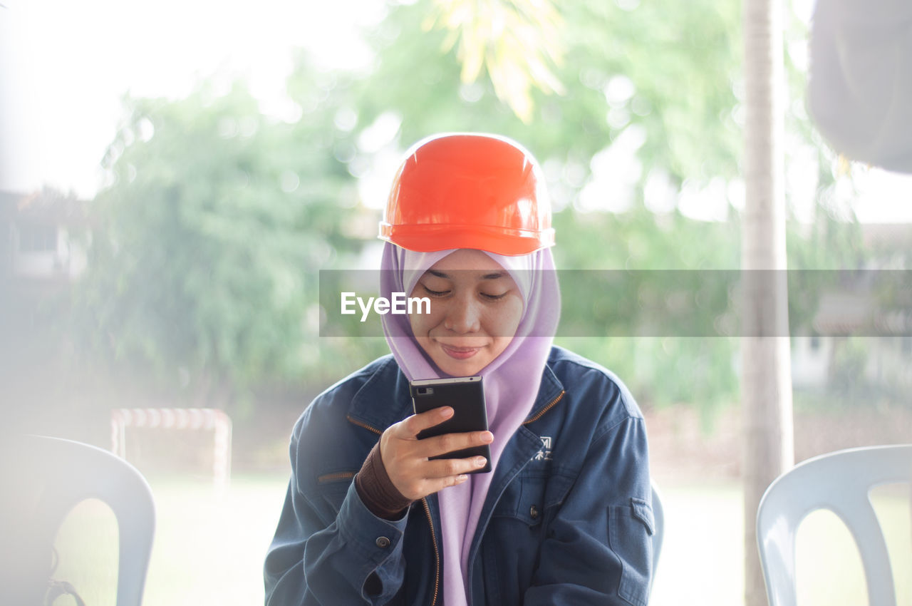 Young woman in hardhat using mobile phone