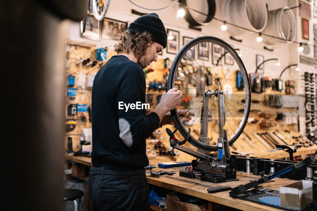 Side view of young male master examining tire on bike wheel while working in professional repair service workshop