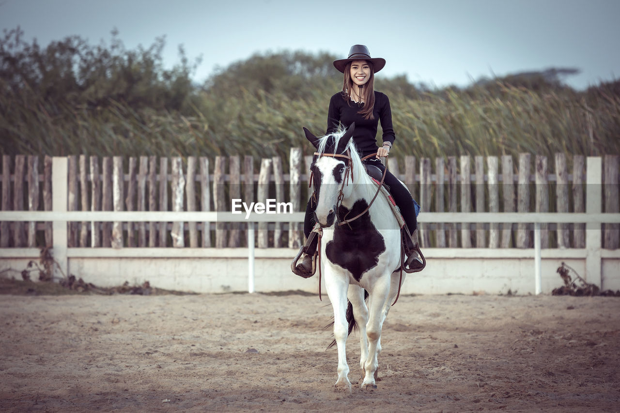 Portrait of woman sitting on horse in ranch against sky