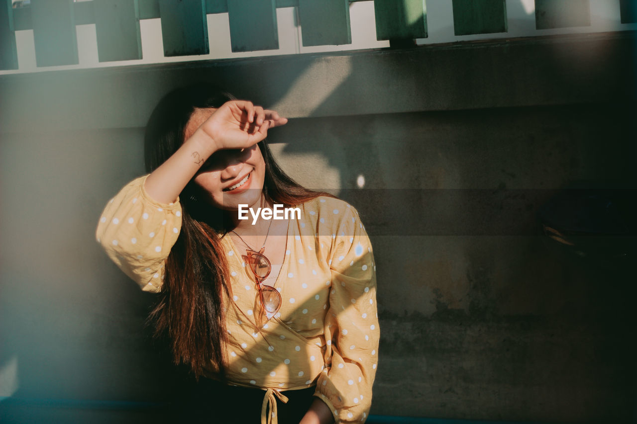 Young woman shielding eyes while standing against wall