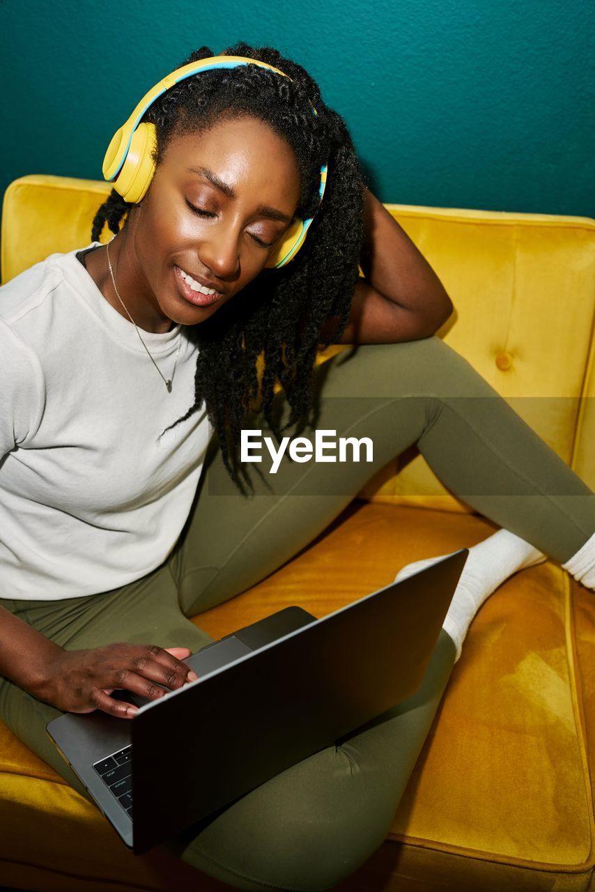 Black styled student woman listening music with yellow earphones