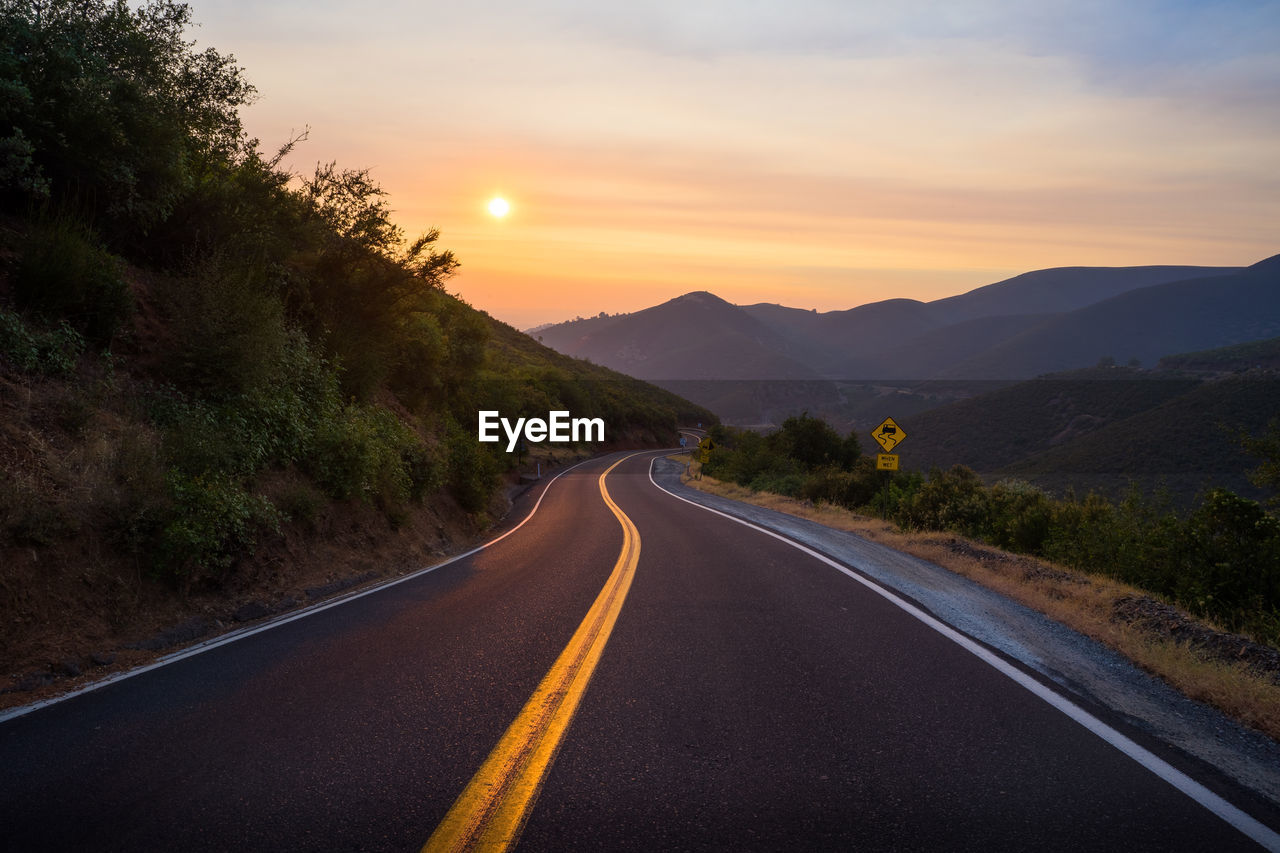 ROAD AMIDST MOUNTAINS AGAINST SKY DURING SUNSET