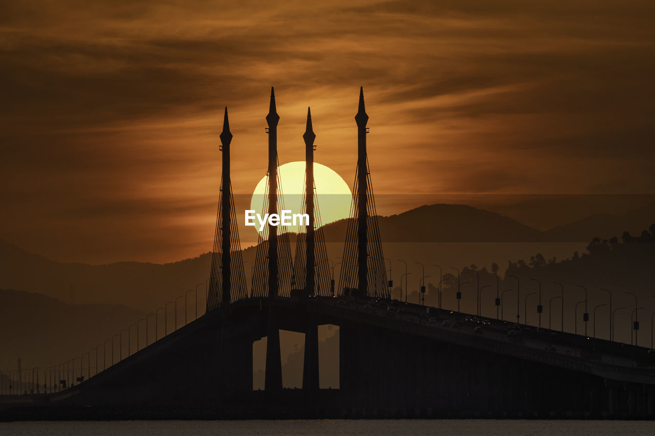 Silhouette penang bridge over sea against sky during sunset