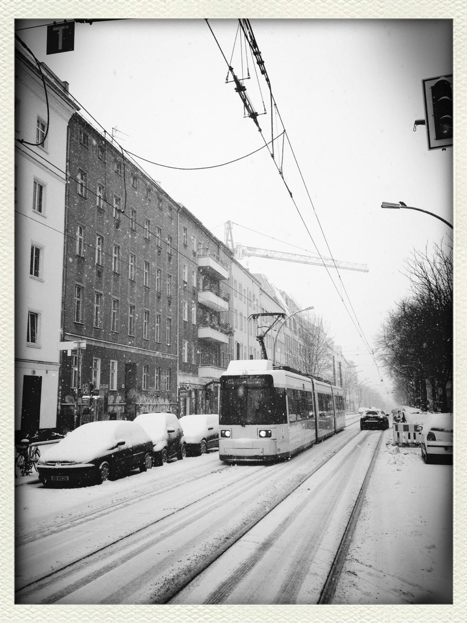 Cable car on snow covered street by buildings against sky