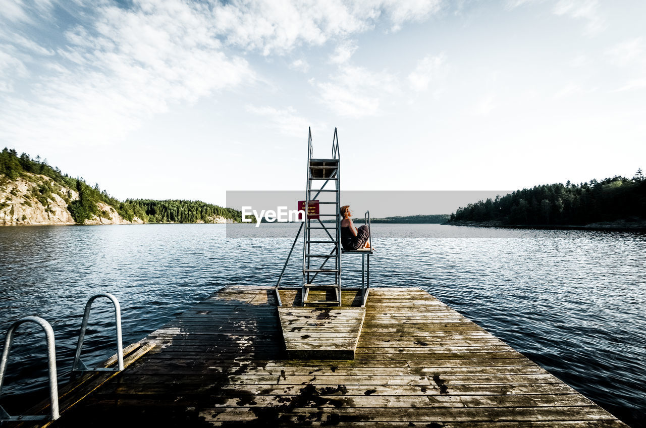 Woman relaxing by diving platform by lake