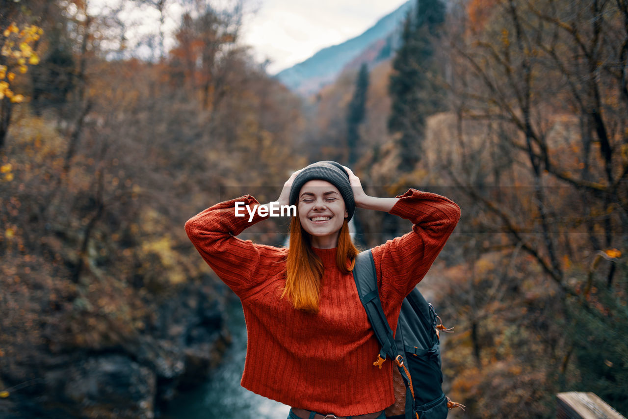 PORTRAIT OF SMILING YOUNG WOMAN STANDING IN PARK