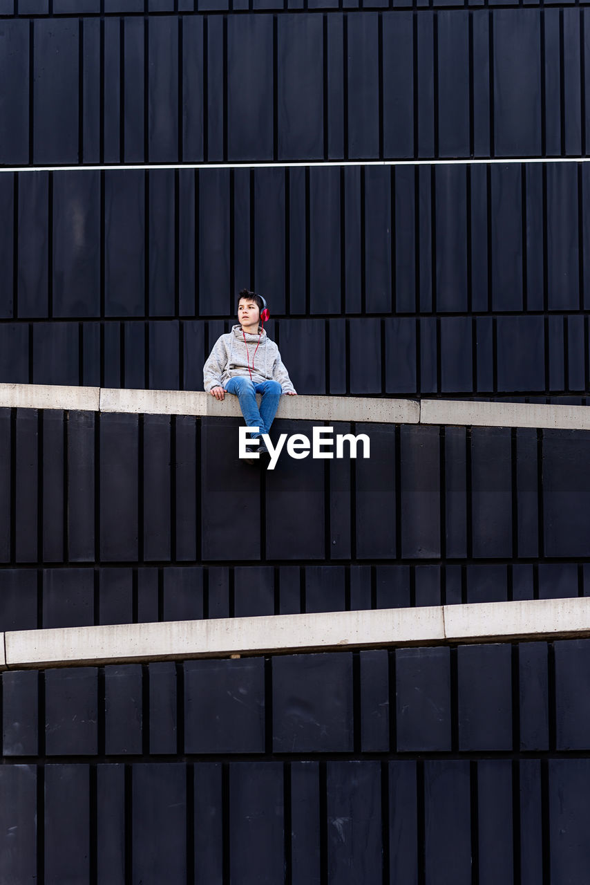 Young teen sitting on a fence while using headphones to listen music