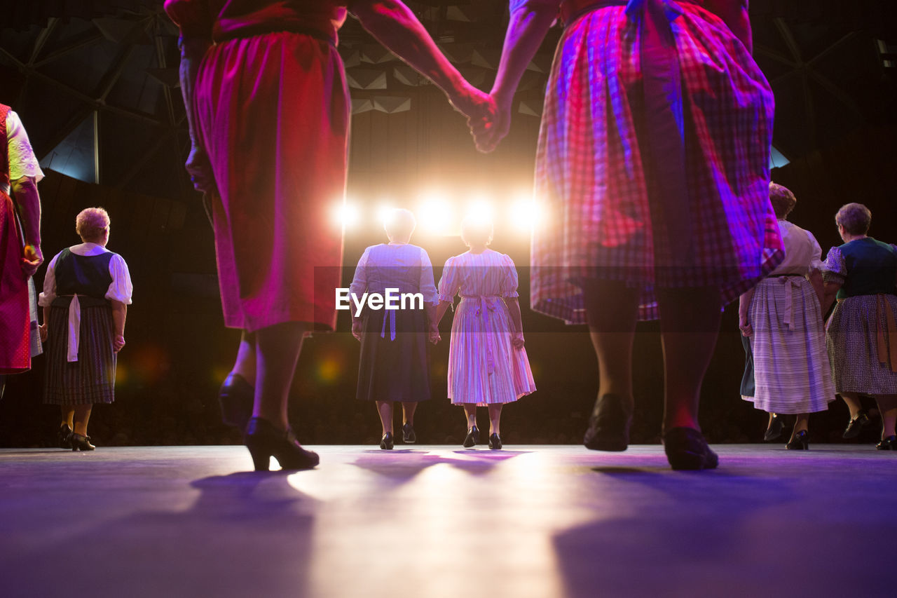 Rear view of women holding hands while standing on stage