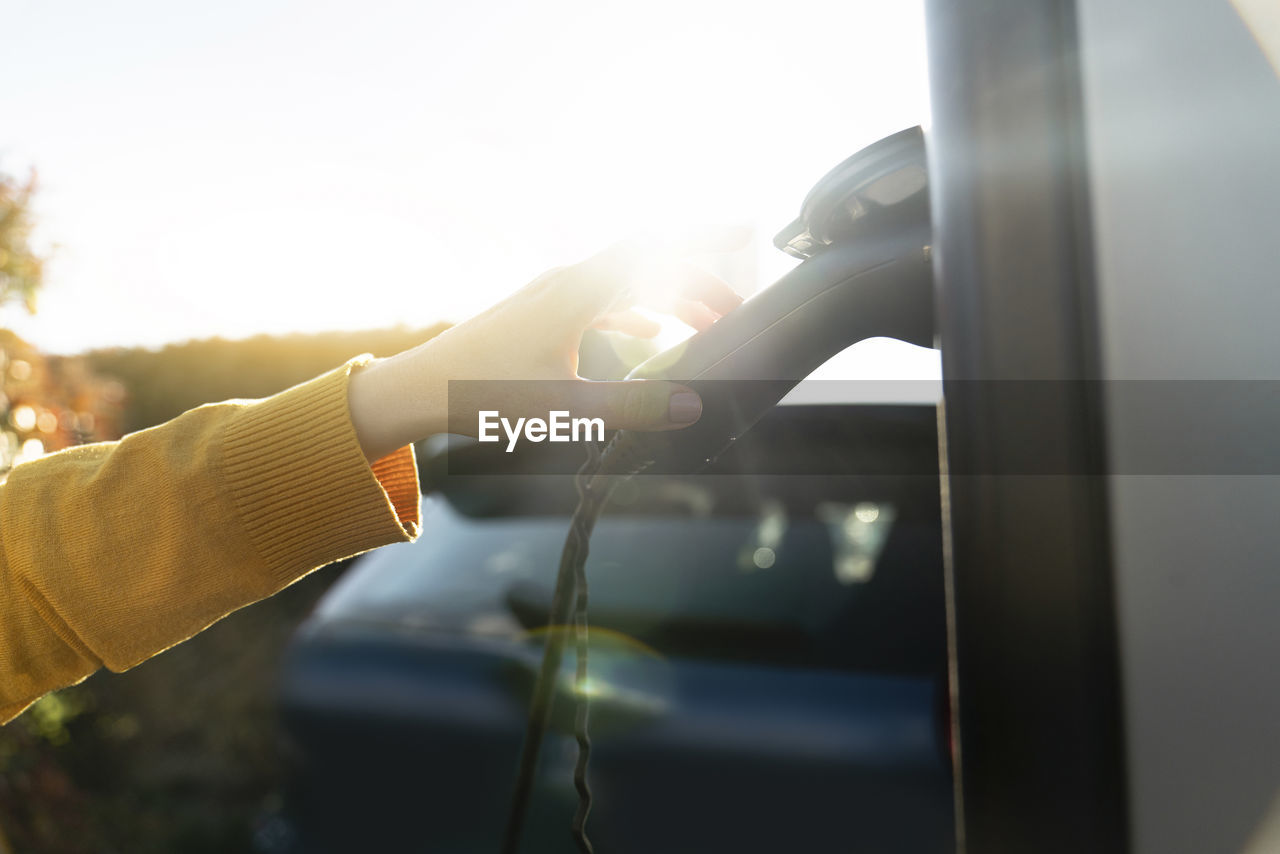 Hand of woman touching electric plug at vehicle charging station