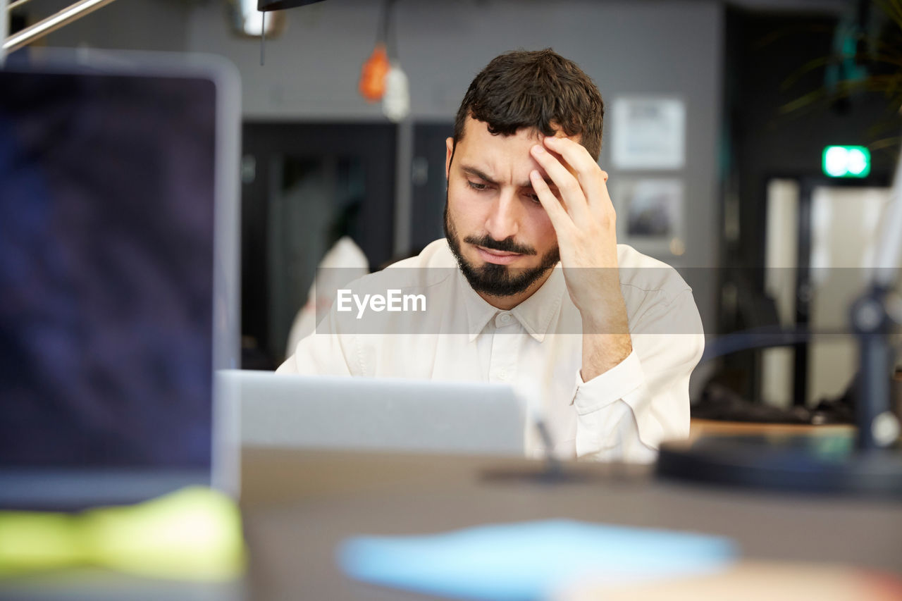Stressed male entrepreneur looking at laptop while sitting in office