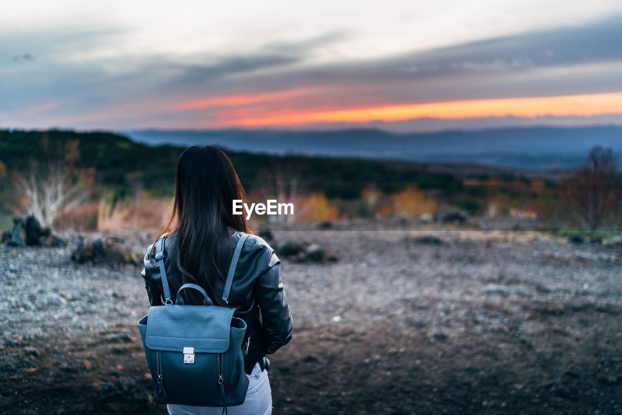 Rear view of woman standing on field against sky during sunset