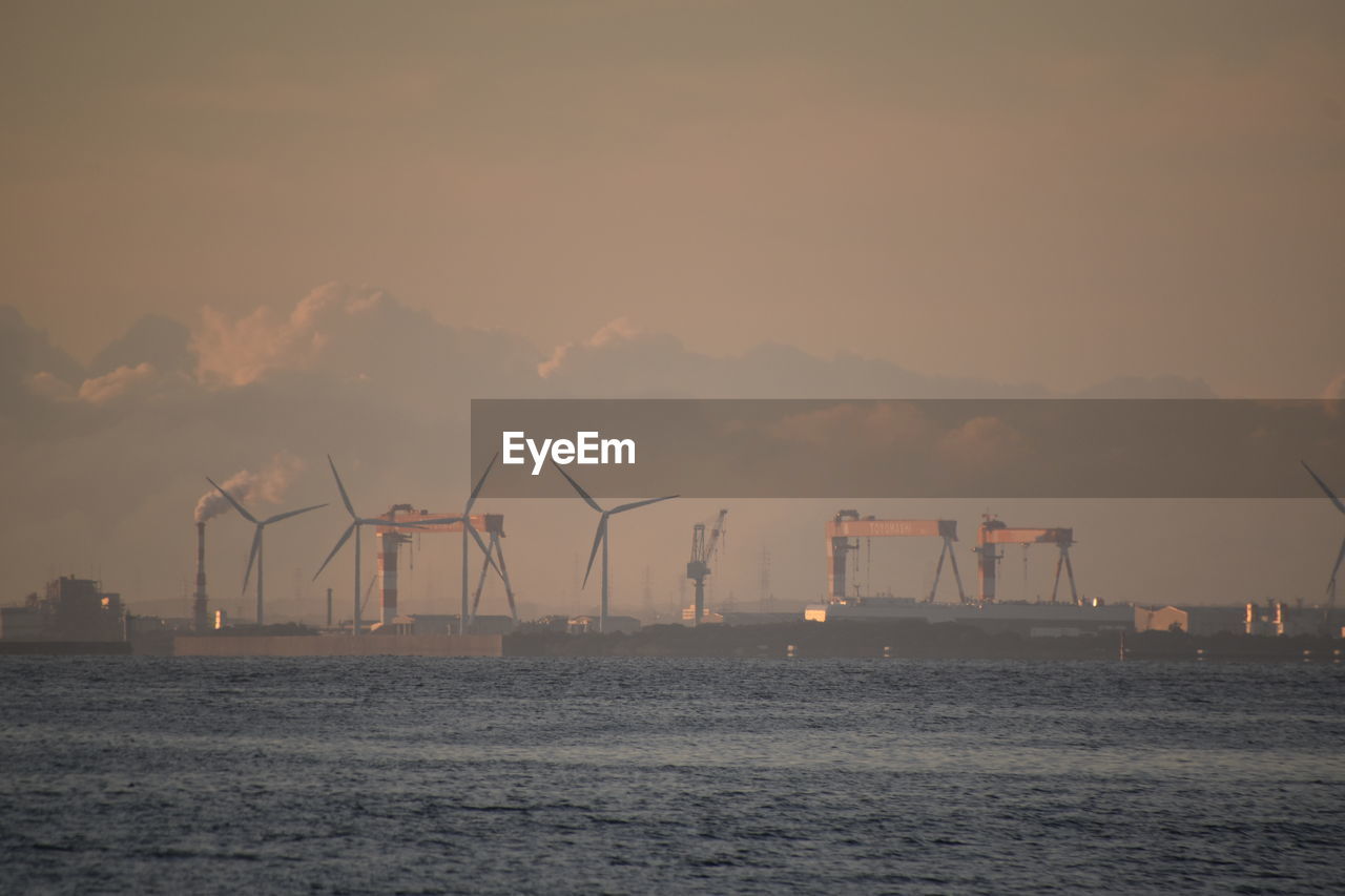 Cranes at commercial dock against sky during sunset