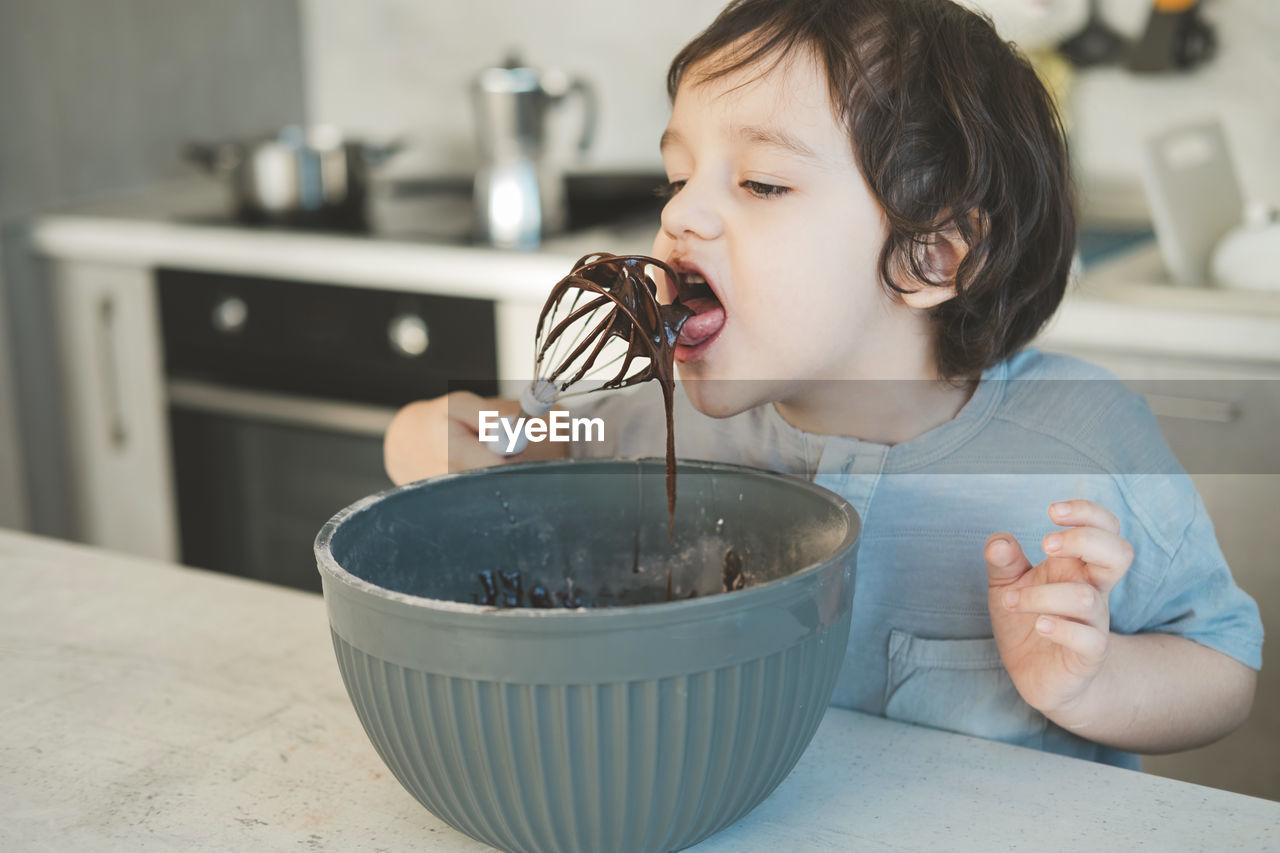 Boy licking chocolate in kitchen