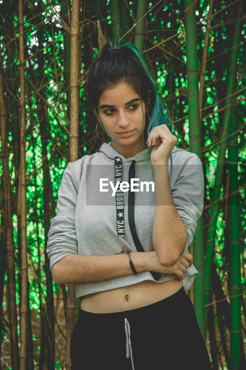 Thoughtful young woman looking away against trees in forest