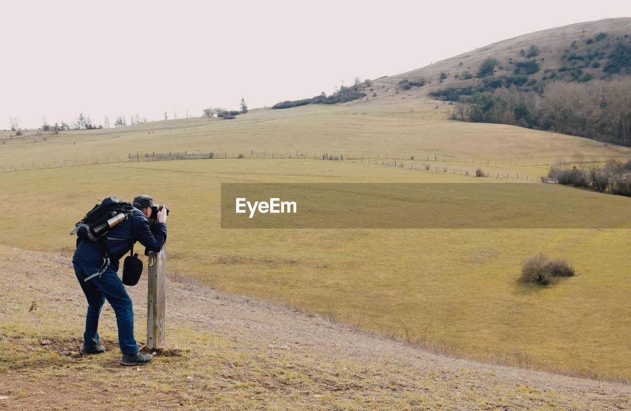 Full length side view of backpacker photographing on landscape