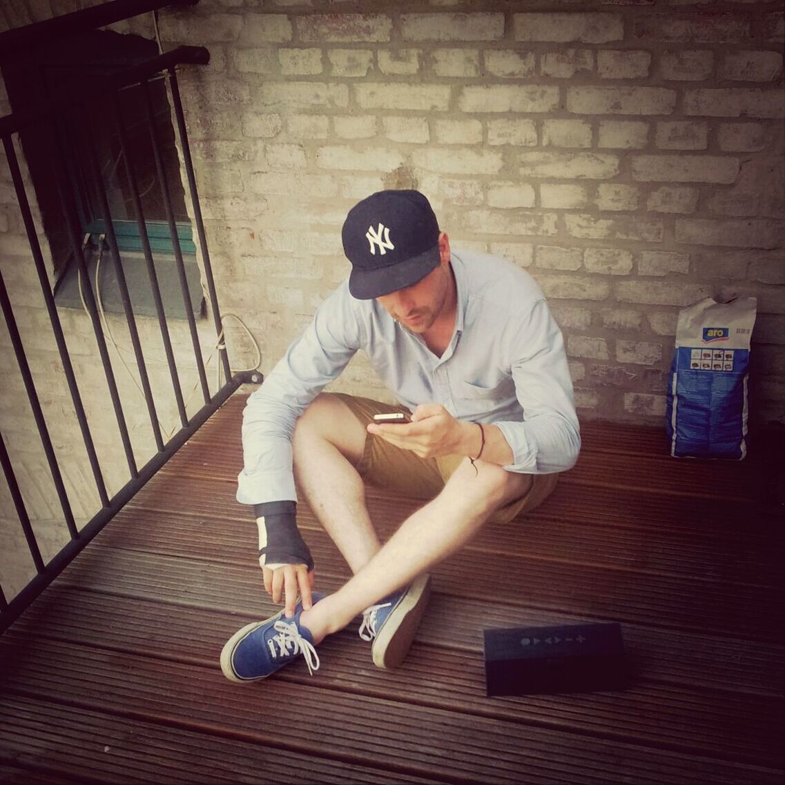 A young man sitting on a terrace texting on a smartphone