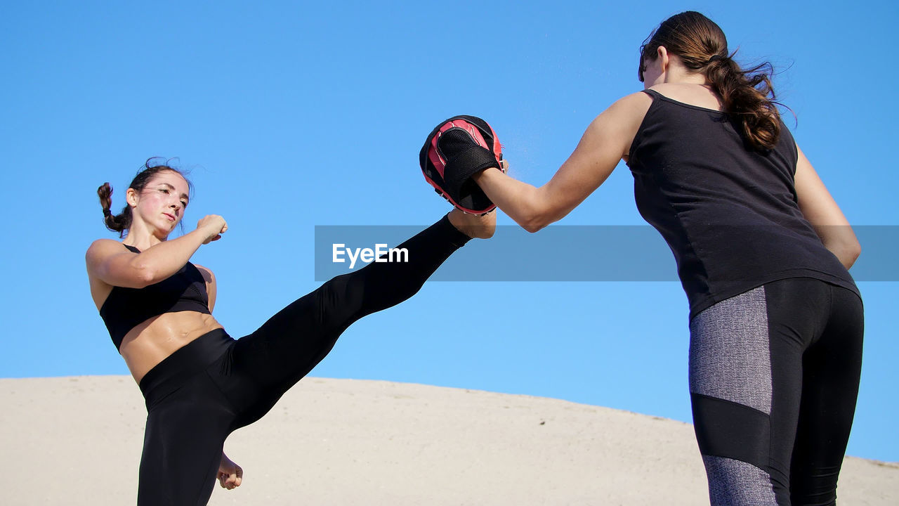 Two athletic, young women in black fitness suits are engaged in a pair work out kicks train to fight