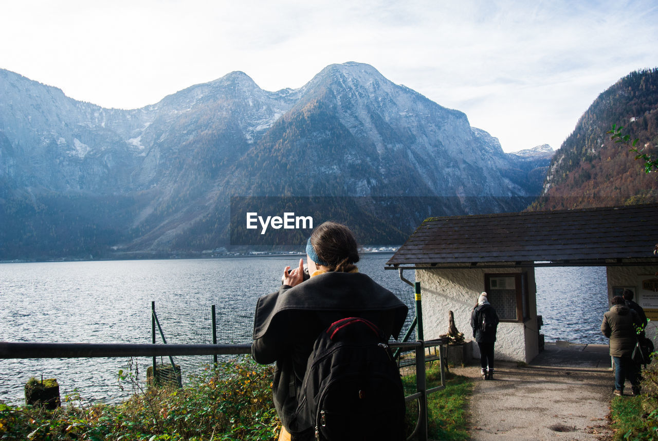 Rear view of friends standing by lake against mountains