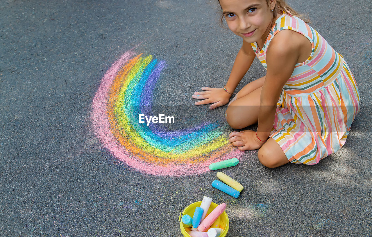Girl drawing rainbow with chalk on sidewalk