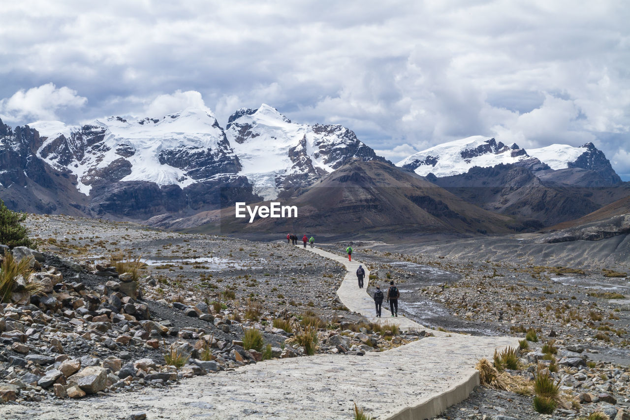 People walking on footpath against snowy mountains