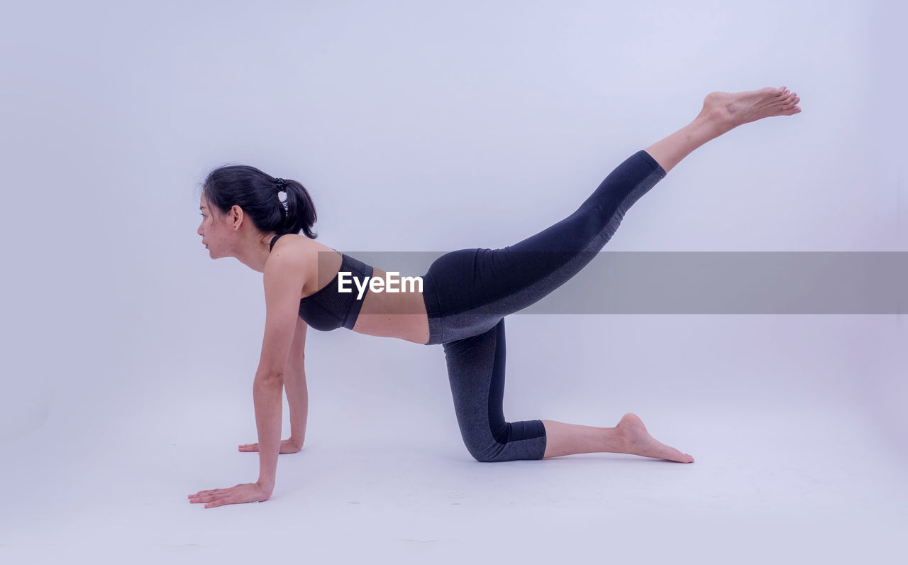 Side view of woman doing yoga against white background