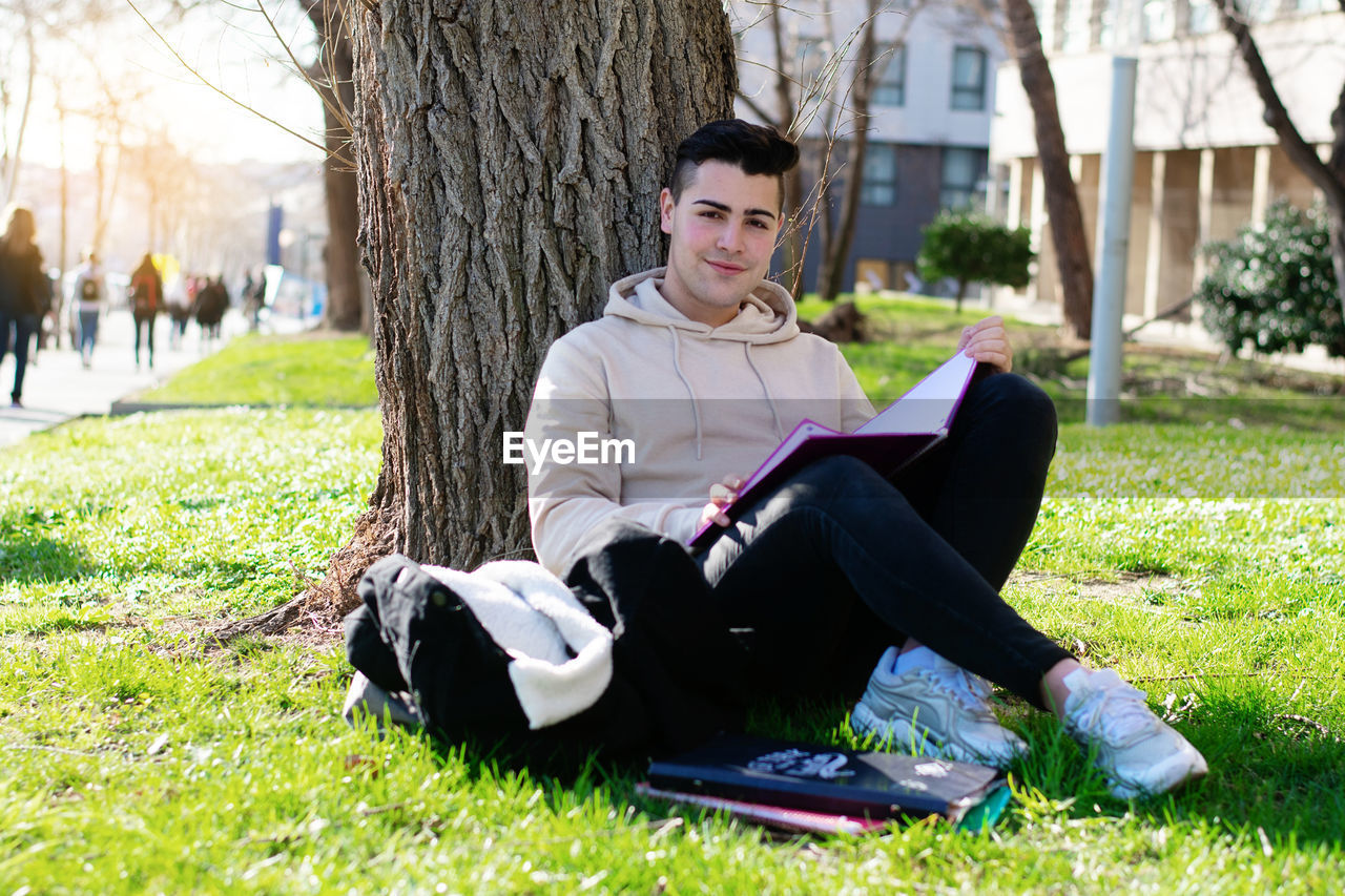 YOUNG MAN SITTING ON TREE TRUNK BY GRASS