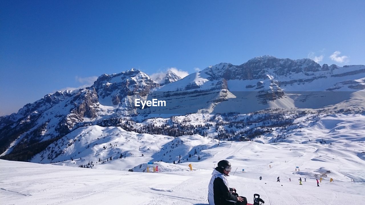 Young man looking away while sitting on snow covered land