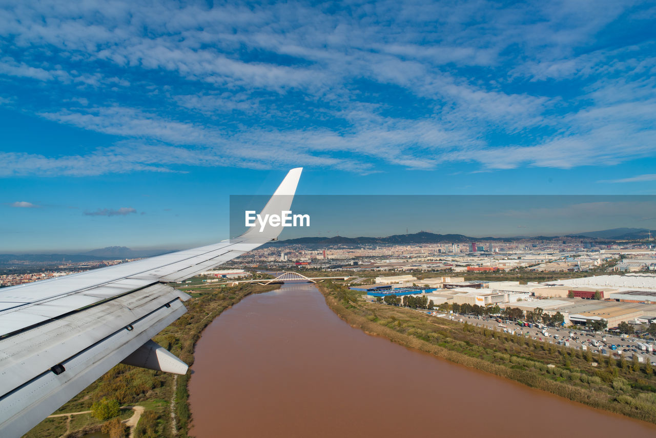 Cropped image of airplane wing overlooking cityscape against cloudy sky