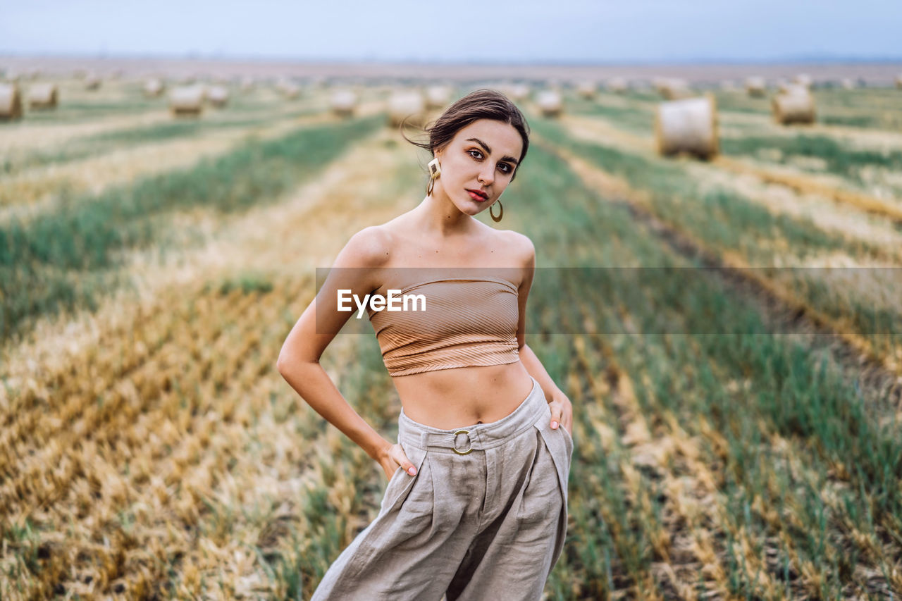 Smiling woman in sunglasses with bare shoulders on a background of wheat field and bales of hay.