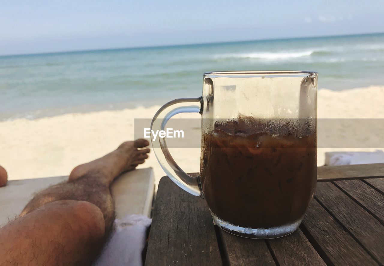 Low section of man with iced coffee against sea
